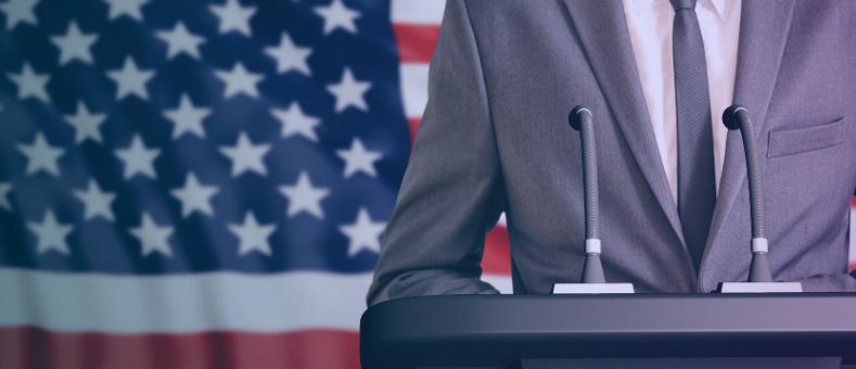 Image of man at podium with american flag in background